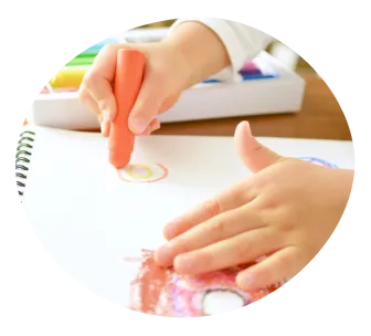 橙色のクレヨンを持って絵を描く子どもの手元の写真